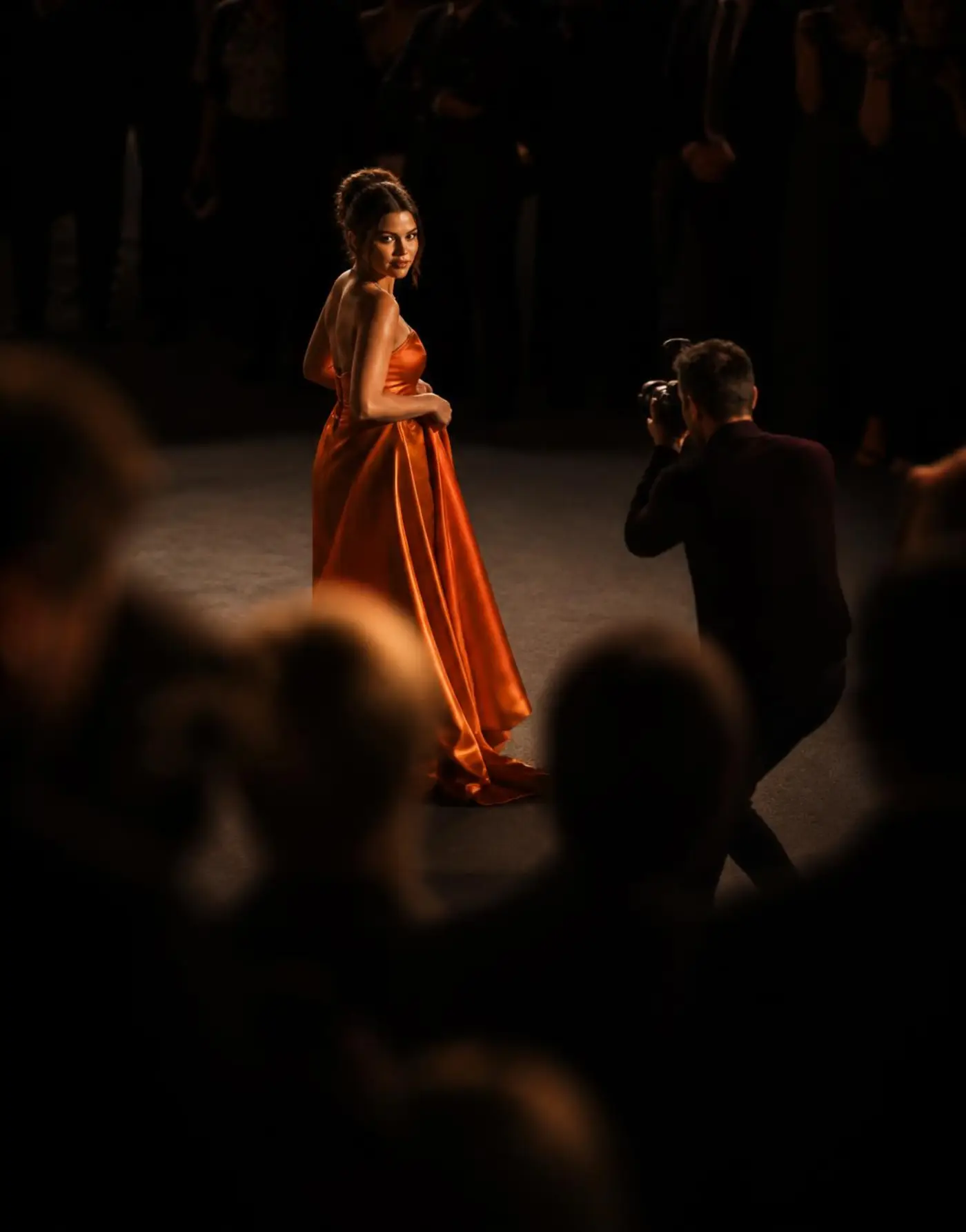 A photographer shooting a guest in an ember gown surrounded by a darkened crowd